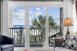 Un balcon avec vue sur la plage, une chaise, une table et une lampe.