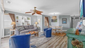A living room with a grey sofa, blue armchairs, a wooden coffee table, and a dining area with a white table and chairs. - *Fall into Savings-20% Off New Bookings thru 2026* (Surfside Beach)