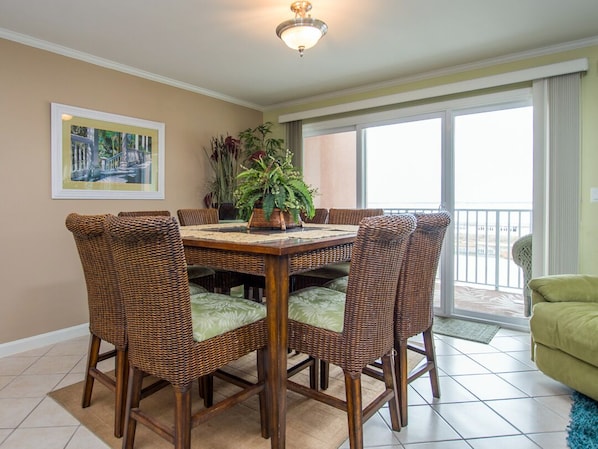 A dining area with a wooden table and wicker chairs, a potted plant, and a balcony with a view.