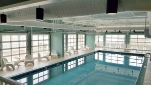 A large indoor swimming pool with multiple lanes, surrounded by white lounge chairs and tables. - Bayfront unit. Walk to the Convention Center, dining, shops and the beach. (Ocean City)