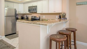 A kitchen with white cabinets, a stainless steel refrigerator, a microwave, and a coffee maker. There are three wooden stools at the island. - Bayfront unit. Walk to the Convention Center, dining, shops and the beach. (Ocean City)