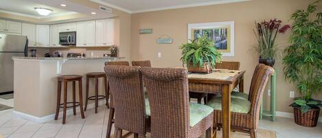 A kitchen with white cabinets, a microwave, and a refrigerator. There is a dining area with wicker chairs and a table.