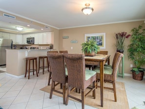 A kitchen with white cabinets, a microwave, and a refrigerator. There is a dining area with wicker chairs and a table.