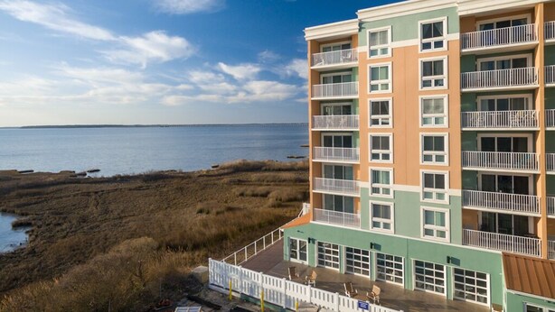 A multi-story hotel with balconies, a view of the beach, and a parking area. - Bayfront unit. Walk to the Convention Center, dining, shops and the beach. (Ocean City)