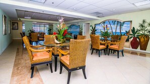 A dining area with wicker chairs and a glass table, surrounded by potted plants and a mural of a beach scene. - Bayfront unit. Walk to the Convention Center, dining, shops and the beach. (Ocean City)