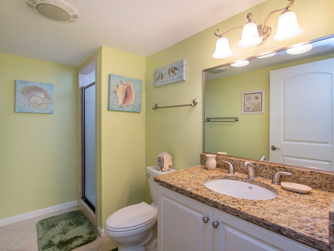 A bathroom with a granite countertop, white sink, and a large mirror. There are wall-mounted towel racks and framed artwork above the mirror.