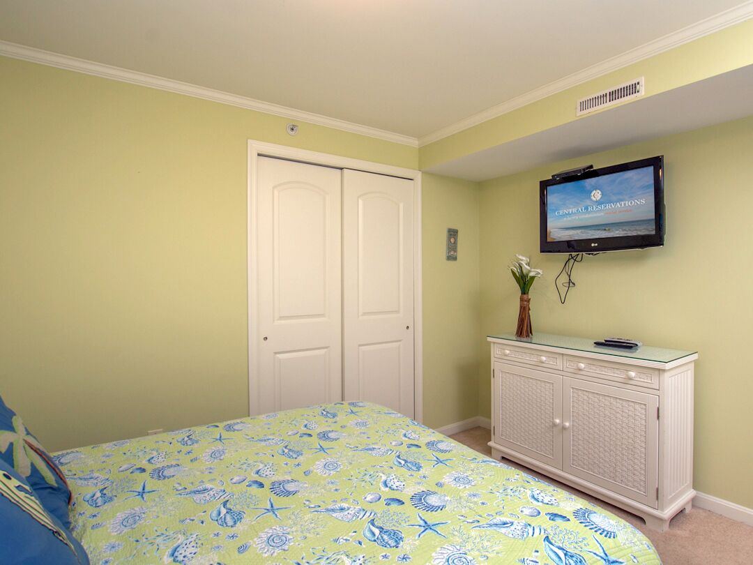 Een slaapkamer met een bed, een aan de muur bevestigde televisie en een witte kast.