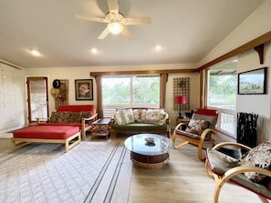 Un salon spacieux doté d’un ventilateur de plafond, d’un canapé rouge, d’un canapé vert, d’une table basse ronde et d’une chaise en bois.
