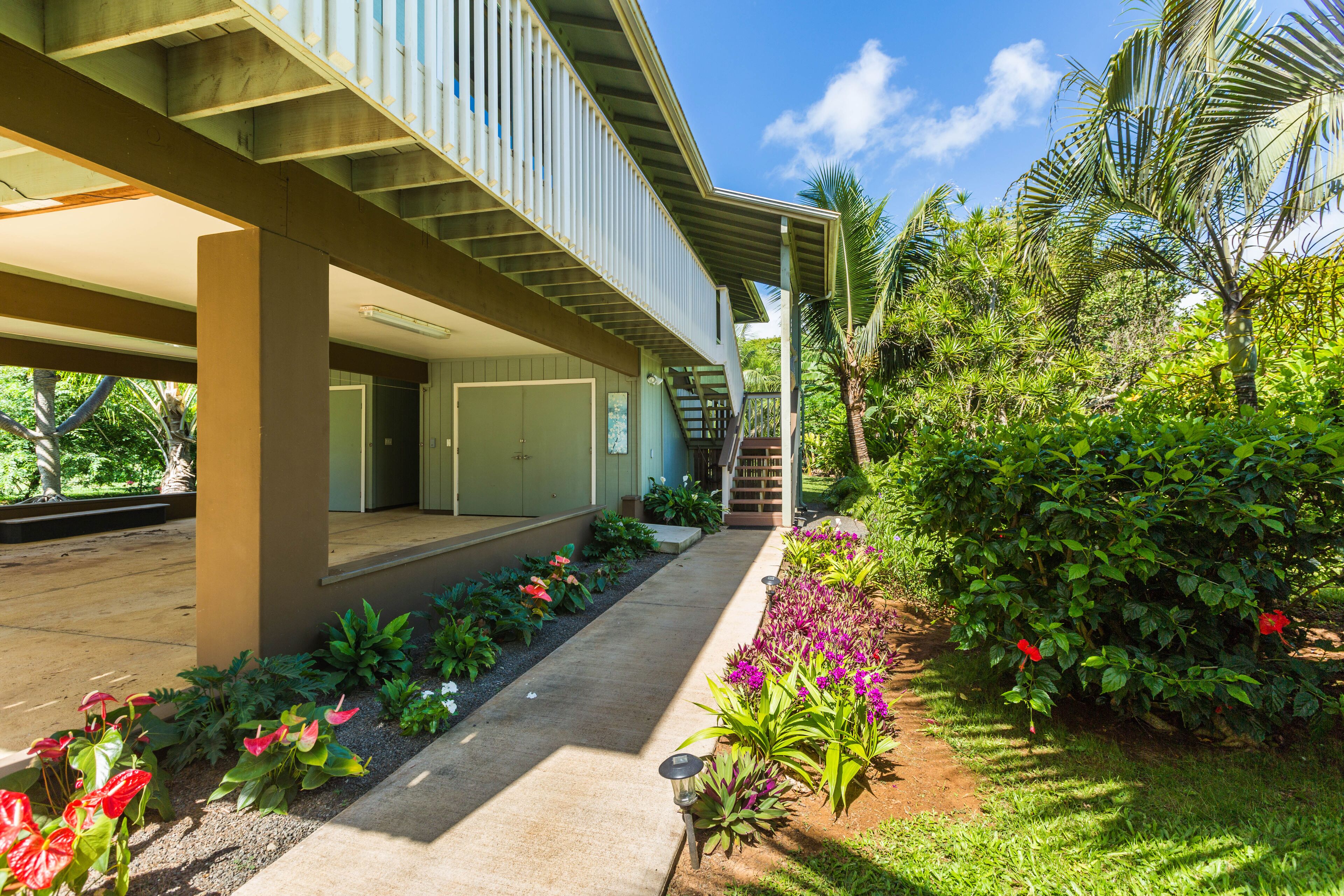 A modern building with a covered outdoor area, a concrete pathway, and lush greenery.