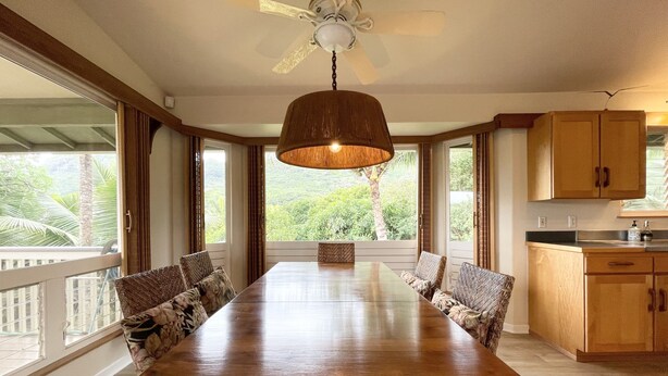 Un'ampia sala da pranzo con un lungo tavolo in legno, sedie in vimini e una ventola a soffitto.