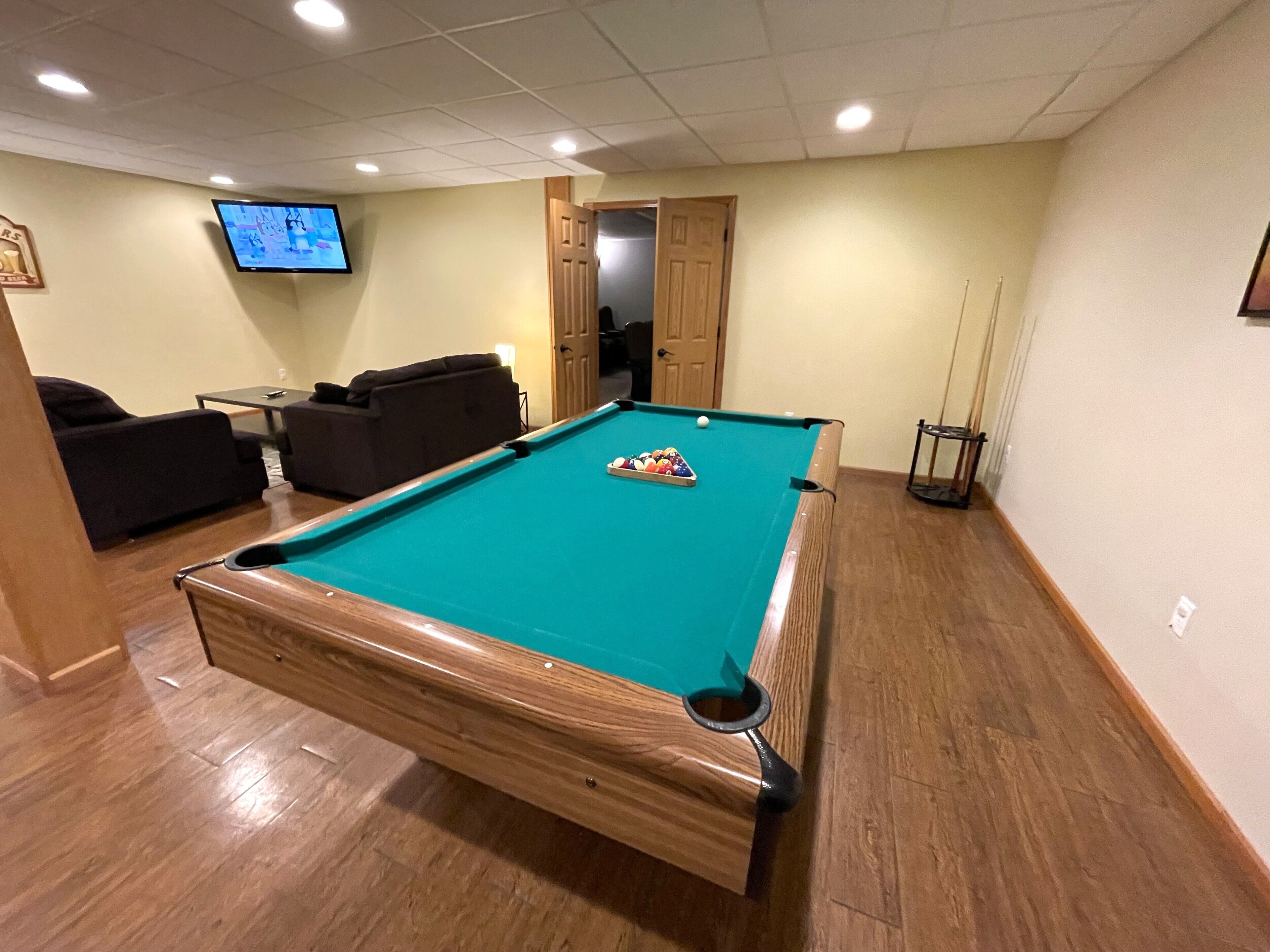 Une table de billard avec des billes, un téléviseur, un canapé et une porte donnant sur une autre pièce.