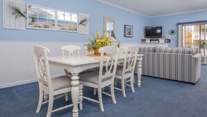 Un coin repas avec une table et des chaises blanches, un canapé à rayures et un téléviseur fixé au mur.