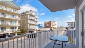 Un balcon avec une table, donnant sur une rue bordée de nombreux immeubles, dont un hôtel.