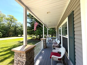 A covered porch with stone pillars, white wicker chairs, and an American flag.