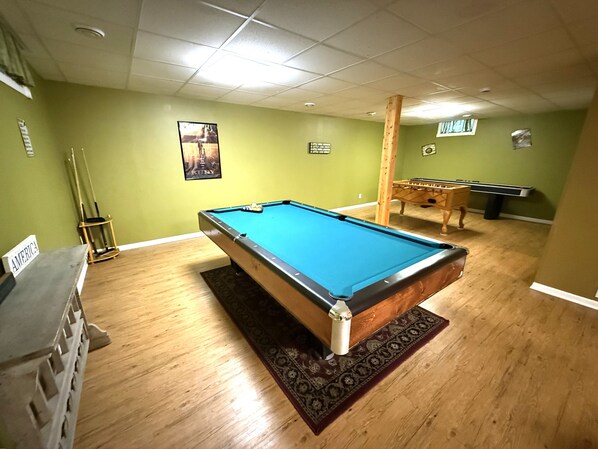 A pool table in a room with green walls, a wooden floor, and a ceiling with recessed lighting.