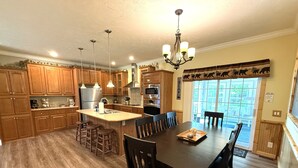 A kitchen with wooden cabinets, a central island, bar stools, a dining table with chairs, and a chandelier.