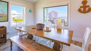 A dining area with a wooden table and benches, large windows with ocean views, and a wicker basket on the table.