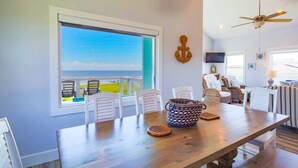 A dining area with a wooden table, chairs, and a view of the ocean.