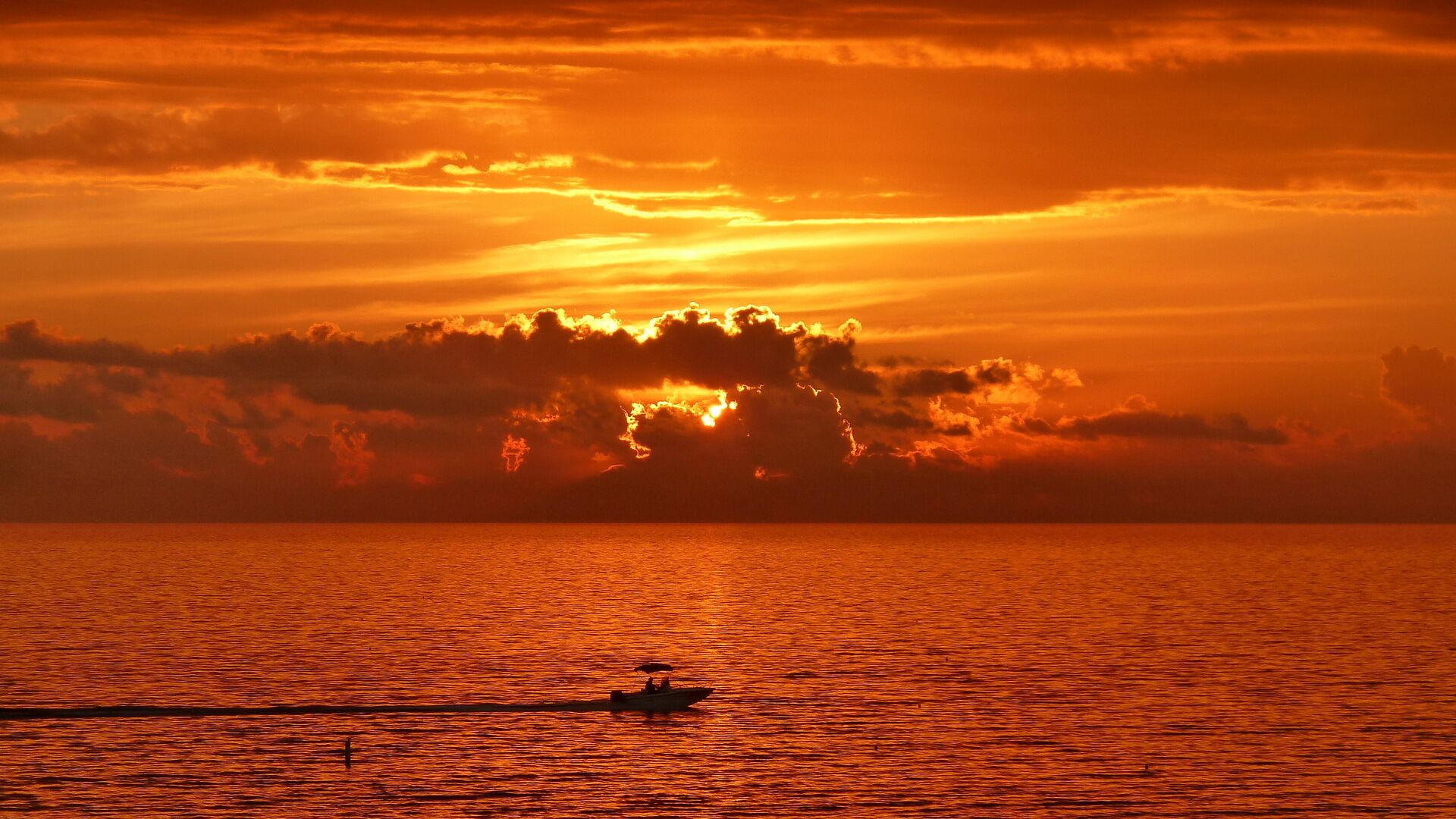 Ein Sonnenuntergang über einem ruhigen Meer, im Vordergrund ein Boot.