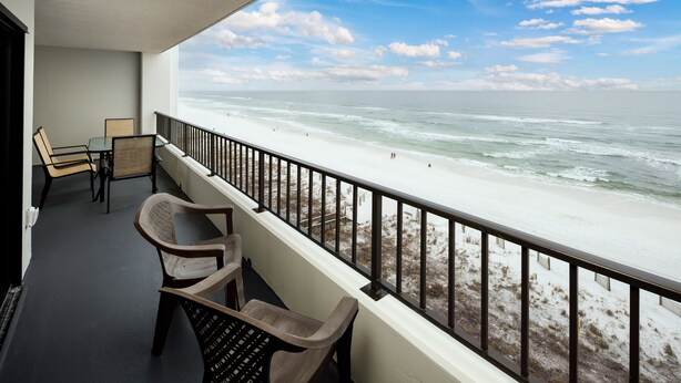 Een balkon met uitzicht op het strand, met twee rieten stoelen en een tafel.