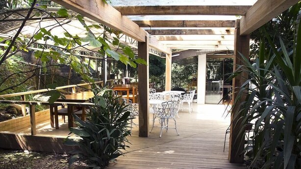 An outdoor patio area with wooden flooring, metal chairs, and tables. - Pousada Villa Dei Fiori (Bento Gonçalves)