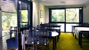 A dining area with multiple tables and chairs, large windows with a view of greenery, and a yellow carpet. - Pousada Villa Dei Fiori (Bento Gonçalves)