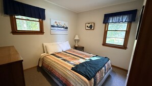 A bedroom with a bed, two windows with curtains, a nightstand with a lamp, and a painting on the wall. - Cozy cottage Big Glen Lake, Tennis Court, Dock, Kayaks, Rowboat, Sunset view (Maple City)