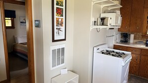 A compact kitchen with a stove, microwave, and wooden cabinets. - Cozy cottage Big Glen Lake, Tennis Court, Dock, Kayaks, Rowboat, Sunset view (Maple City)
