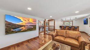 A spacious living room with a large painting of a sunset over a lake, a leather sofa, and a wooden coffee table. - Heavenly Mountain View: Pool Table, Hot Tub, BBQ (South Lake Tahoe)