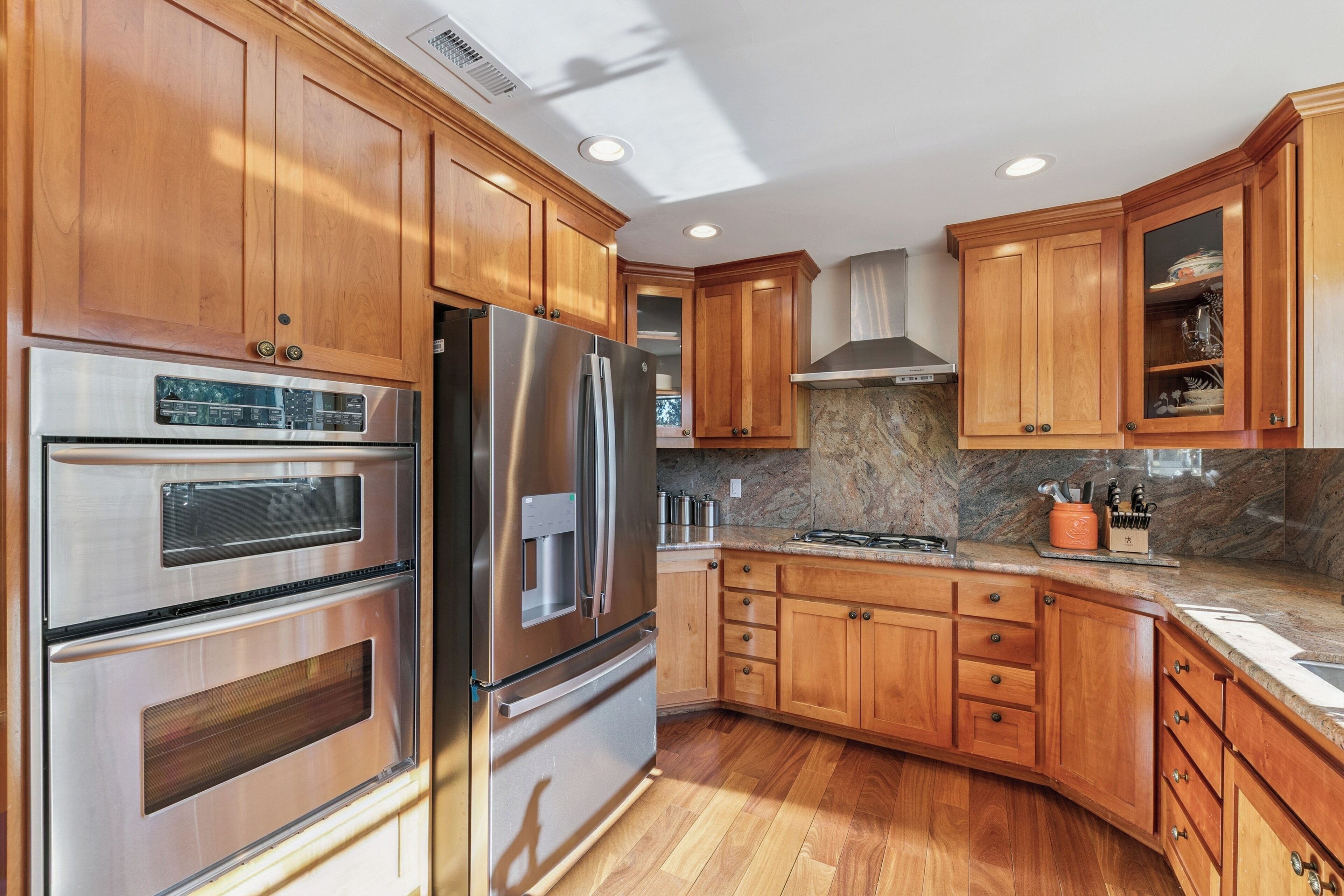 A kitchen with wooden cabinets, stainless steel appliances, granite countertops, and a built-in oven.