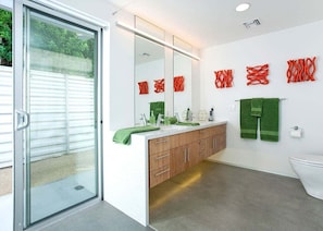Un baño moderno con puerta de cristal, espejo grande, armarios de madera y toallas verdes.