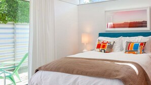 A hotel room with a bed, a window with curtains, a chair, and a painting on the wall.