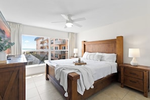 A bedroom with a wooden bed, bedside tables, a ceiling fan, and a view of a building through the window.
