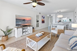 A modern living room with a wooden coffee table, white sofas, and a large painting of a sunset.