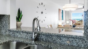 Una cocina moderna con encimeras de granito, un lavamanos de acero inoxidable y un reloj montado en la pared.