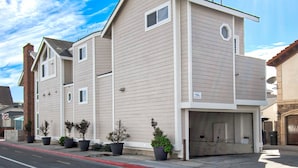A two-story residential building with a garage, multiple windows, and potted plants along the sidewalk. - Awesome lower unit in a duplex just one house away from the sand and boardwalk! (Newport Beach)