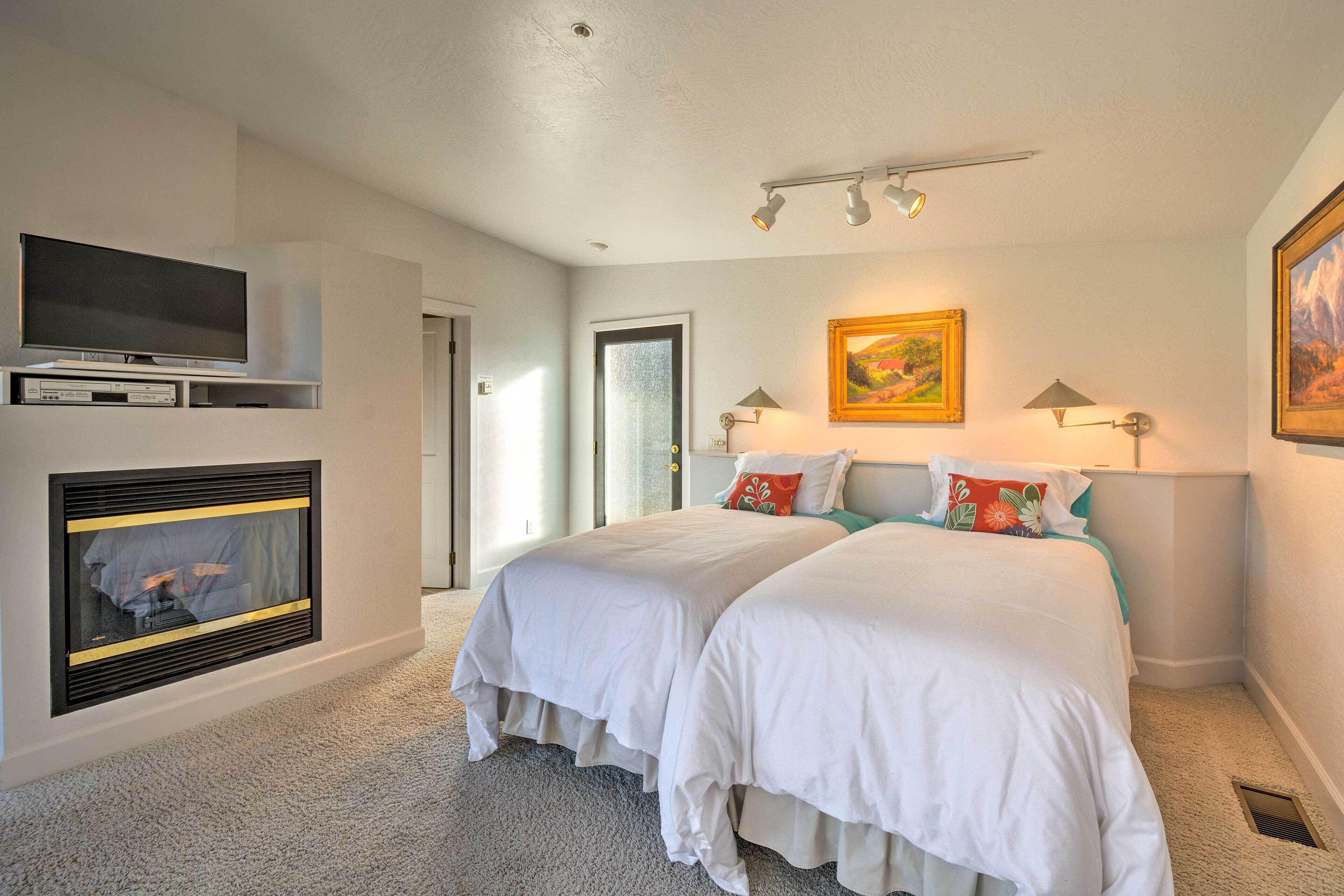 A hotel room with two beds, a flat-screen TV, a fireplace, and artwork on the walls.