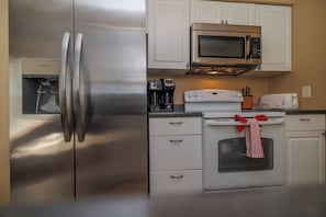 A kitchen with a stainless steel refrigerator, a microwave, a coffee maker, an oven, and white cabinetry.