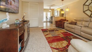 A living room with a ceiling fan, a TV, a fireplace, and a dining area in the background. - Relaxing Tropical Pool Home Close to Beach and Disney (Titusville)