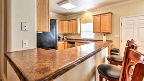 A kitchen with wooden cabinets, a granite countertop, and a black refrigerator. - Waterfront Corpus Christi Townhome w/ Pool & Dock! (Corpus Christi)