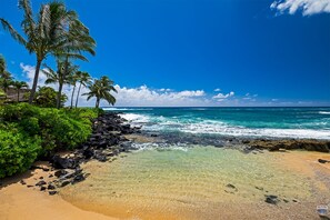 Une plage à l’eau turquoise et limpide, bordée d’une côte rocheuse et ponctuée de palmiers.