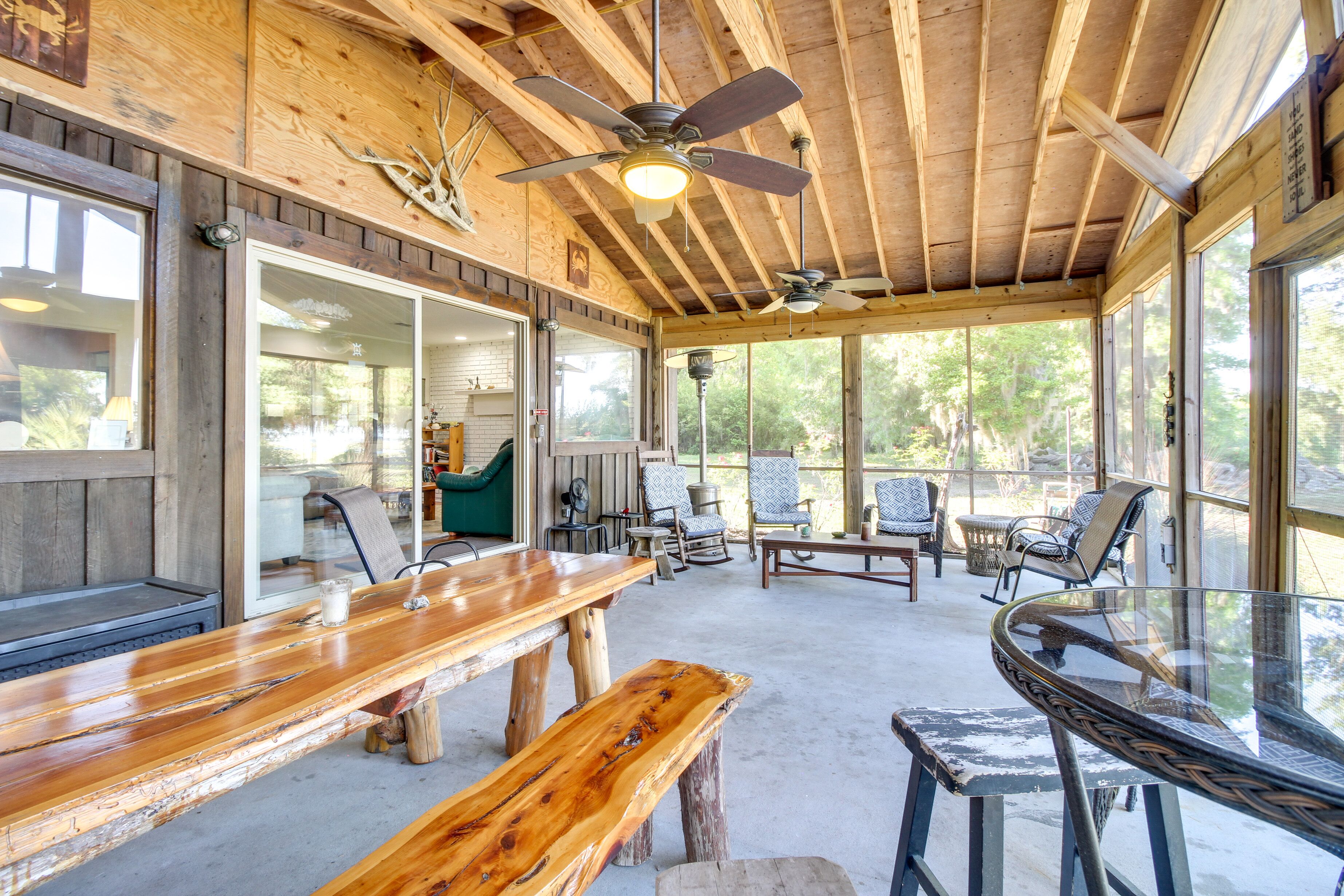 Un vaste patio aménagé avec des meubles en bois, des ventilateurs de plafond et de grandes fenêtres offrant une vue sur l’extérieur.