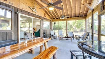 Un vaste patio aménagé avec des meubles en bois, des ventilateurs de plafond et de grandes fenêtres offrant une vue sur l’extérieur.