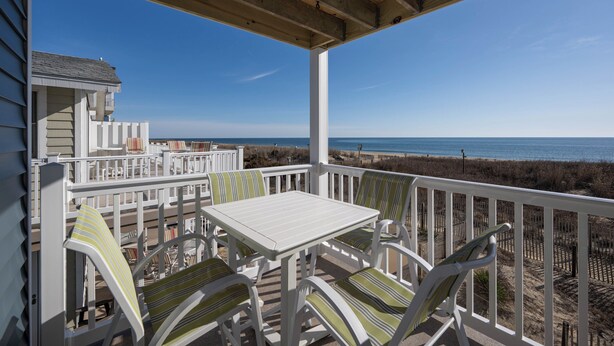 A covered outdoor seating area with a table and chairs, overlooking a beach. - Cozy 3 bedroom, 1.5 bathroom condo located on on 122nd Street and oceanfront (Ocean City)
