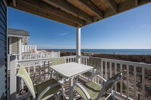 Ein überdachter Außenbereich mit Tisch und Stühlen, mit Blick auf einen Strand.