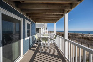 Ein überdachter Balkon mit Blick auf den Strand, weiße Geländer und ein Tisch mit Stühlen.