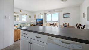 A kitchen with a countertop, cabinets, a dishwasher, a dining table with chairs, a television, and a window with a view. - Cozy 3 bedroom, 1.5 bathroom condo located on on 122nd Street and oceanfront (Ocean City)