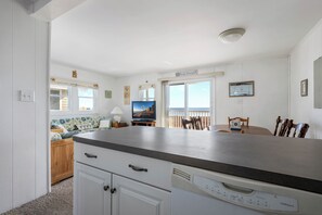 A kitchen with a countertop, cabinets, a dishwasher, a dining table with chairs, a television, and a window with a view.