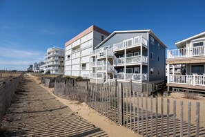 Ein Strandhotel mit mehreren Balkonen, einem Sandweg und einem Holzzaun.