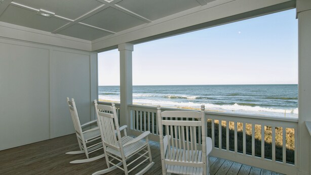 Une terrasse en bois avec deux fauteuils à bascule donnant sur la plage.
